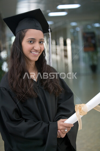 اللباس الأكاديمي الموحد لخرجي الجامعات والمعاهد الدوليه, الاحتفالات بتحقيق حلم النجاح من الجامعة, الفرح والسرور والاحتفال بيوم التخرج بإيماءات السعادة, صورة مقربة لطالبة عربية خليجية إماراتية ترتدي زي التخرج والقبعة تحمل بيدها شهادة التفوق والنجاح