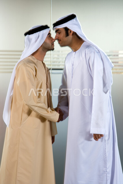 Making successful business deals and agreeing on new projects, shaking hands between friends and colleagues in the work environment in the United Arab Emirates, two Arab Gulf businessmen wearing Emirati ghutras and kandoras and kissing the nose traditiona
