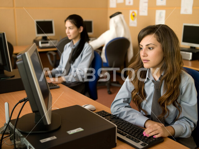 Active participation of students, teaching students how to use a computer in school, Emirati Gulf Arab students wearing school uniforms doing work and learning in the computer lab, e-learning and curricula developed in UAE schools.