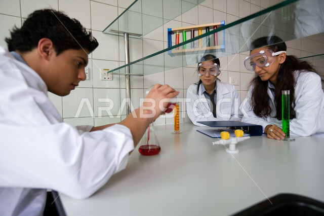  الخبرة والاستفادة من التطبيق العملي في المخابر الكيميائية، التجارب العلمية الحديثة وتطور طرق التعلم، مجموعة من الزملاء العربيين الخليجين الاماراتيين يرتدون نظارات الحماية ويقومون بتجربة علمية كيميائية في مخبر المدرسة 