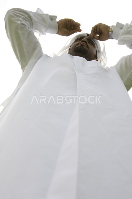 ايماءات يدين للاحتماء من اشعة الشمس, الوقوف باستقامه ورجوله ، صوره من الأسفل لرجل اماراتي عربي خليجي يرتدي الكندوره والشماغ الابيض يقف بثقه ، النظر الى شيء ما في الخارج تحت اشعة الشمس في وضح النهار، منظر السماء الزرقاء