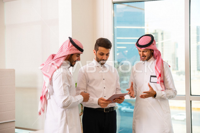 مجموعة من رجال الأعمال الرياديون الخليجيون ، احدهم من جنسية مختلفة يرتدي البدلة الرسمية ، ادارة الاعمال داخل مقر الشركة ، استخدام جهاز التابلت المحمول لاتمام المهام ، شركة سعودية ، بيئة العمل