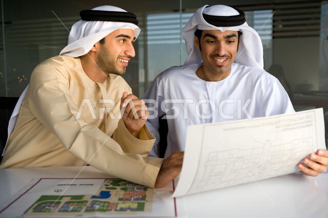 التدقيق والإشراف على مخططات مشروع عقاري، بيئة العمل الإماراتية، اجتماع عمل لرجلان أعمال عربيان خليجيان إماراتيان يرتديان الغترة والكندورة الإماراتية، نقاشات وحوارات حول مخطط خريطة هندسية، مفهوم العمل الجماعي في شركات الإمارات