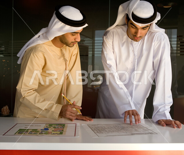 دراسة الخرائط الهندسية لإحدى المشاريع العقارية، رجلان أعمال عربيان خليجيان إماراتيان يرتديان الغترة والكندورة الإماراتية، نقاشات وحوارات عمل إماراتية، بيئة العمل في شركات الإمارات العربية المتحدة