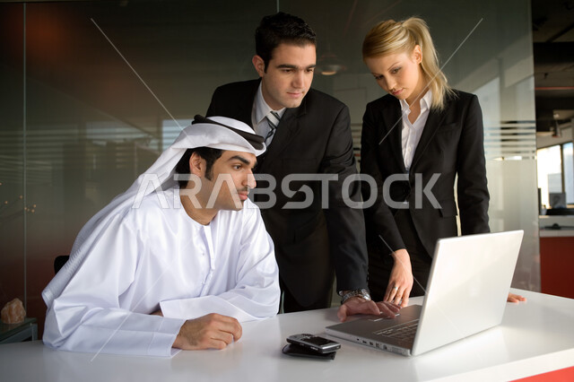 تدريب وتطوير الموظفين في الشركات الإماراتية، رجل وسيدة أعمال أجنبيان يستخدمان الحاسوب المحمول في شرح إستراتيجية العمل مع رجل عربي خليجي إماراتي يرتدي العقال والكندورة الإماراتية، مفهوم الوحدة والعمل الجماعي لتحقيق أهداف الشركة