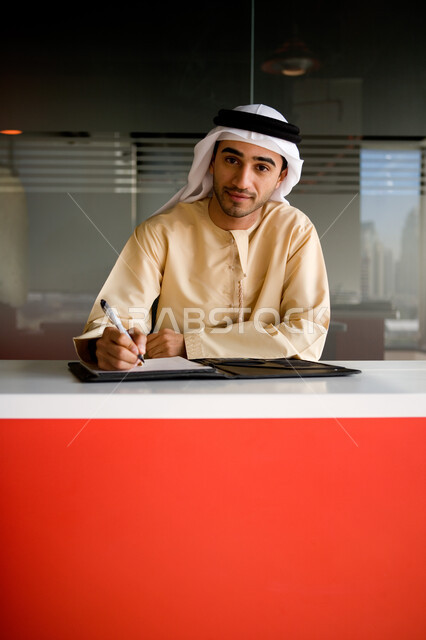 التحقق والتدقيق في شروط عقد عمل جديد، رجل أعمال عربي خليجي إماراتي يرتدي الغترة والكندورة الإماراتية ويقوم بتدوين وكتابة الملاحظات على الورق، دراسة ومراجعة المشاريع، التوقيع على عقود العمل، بيئة العمل في الشركات الإماراتية