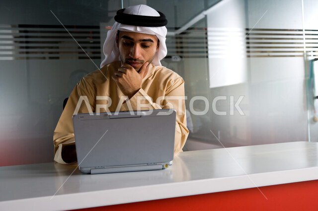 إنجاز وإدارة العمل عن بعد، رجل أعمال عربي خليجي إماراتي يرتدي الزي الإماراتي التقليدي ويقوم بمتابعة المهام اليومية من خلال الحاسوب المحمول، مهن ووظائف مكتبية في الإمارات، شركات عربيه إماراتيه خليجية