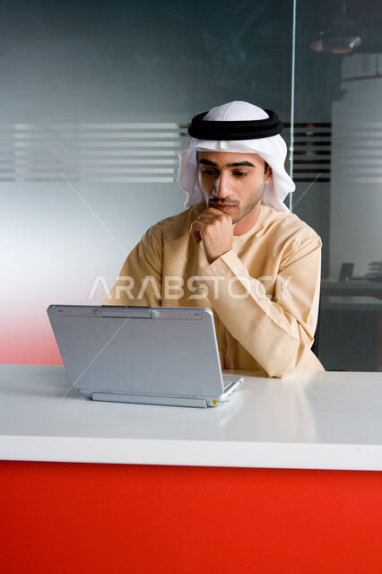 مهن ووظائف مكتبية في الإمارات، إنجاز وإدارة العمل عن بعد، رجل أعمال عربي خليجي إماراتي يرتدي الزي الإماراتي التقليدي ويقوم بمتابعة المهام اليومية من خلال الحاسوب المحمول، شركات عربيه إماراتيه خليجية