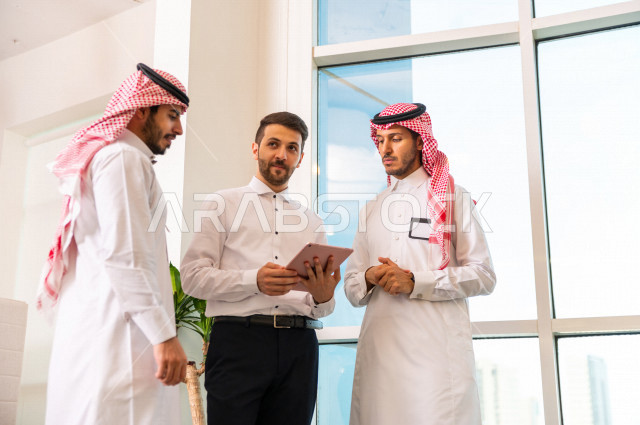 مجموعة من رجال الأعمال الرياديون الخليجيون ، احدهم من جنسية مختلفة يرتدي البدلة الرسمية ، ادارة الاعمال داخل مقر الشركة ، استخدام جهاز التابلت المحمول لاتمام المهام ، شركة سعودية ، بيئة العمل