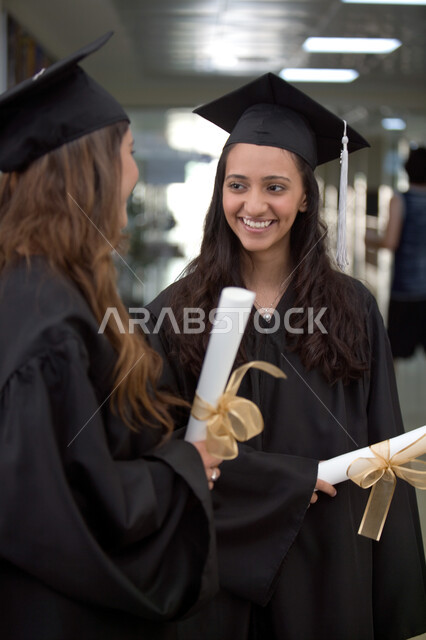 التعليم الجامعي الاماراتي، الاحتفال بالتخرج من الجامعة بإيماءات السعادة والفرح، صورة مقربة لخريجتين عربيتين خليجيتين اماراتيتين مبتسمتين يرتديان ثوب التخرج وتمسكان شهادة التفوق، أهمية الدراسة الجامعية والفرح بتحقيق النجاح 