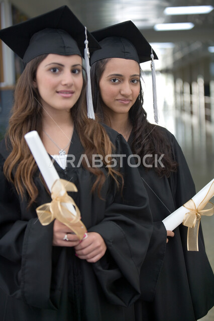 أهمية الدراسة الجامعية والفرح بتحقيق النجاح، التعليم الجامعي الاماراتي، الاحتفال بالتخرج من الجامعة بإيماءات السعادة والفرح، صورة مقربة لخريجتين عربيتين خليجيتين اماراتيتين مبتسمتين يرتديان ملابس التخرج وتمسكان وثيقة التفوق