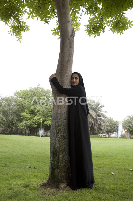  الاستمتاع في التسلية والترفيه في المنتزهات, الاماراتقضاء ممتع في إحدى الحدائق العامة, شابة عربية خليجية إماراتية محجبة تقوم بعناق جذع شجره, اللعب والترفيه في االهواء الطلق, التنزه في الحدائق الخضراء,اللعب في أوقات الفراغ, صورة الجسم بالطول الكامل