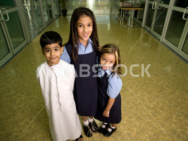 Education in the United Arab Emirates, Emirati Gulf Arab students wearing school uniforms standing in the school corridor, the beginning of a new semester, happiness at returning to schools, looking at the camera, facial gestures indicating happiness, ful