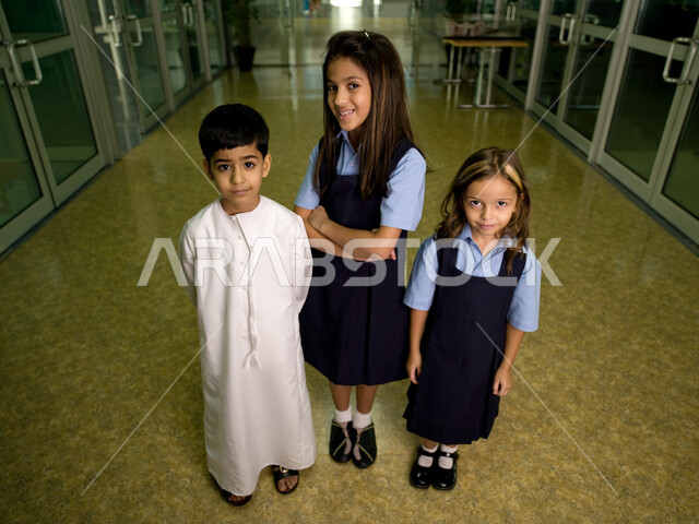 بداية فصل دراسي جديد، التعليم في الإمارات العربية المتحدة، طلاب عرب خليجيون إماراتيون يرتدون الزي المدرسي يقفون في ممر المدرسة, السعادة بالعودة إلى المدارس، النظر إلى الكاميرا، إيماءات وجه تدل على السعادة، صورة الجسم بالطول الكامل.
