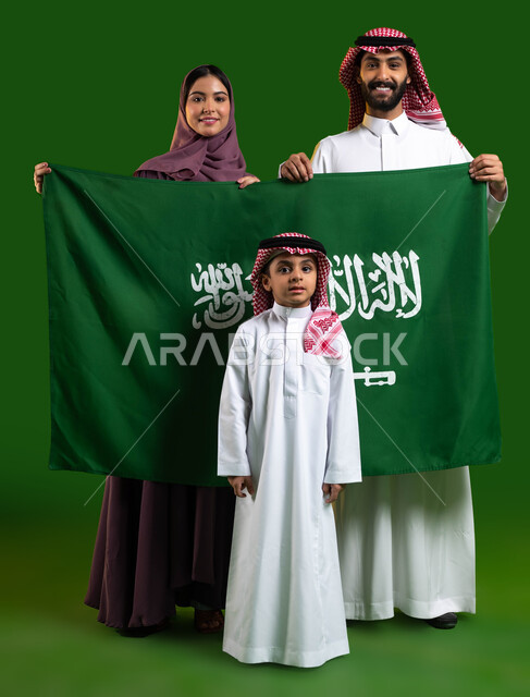 تعليم الابناء حب الوطن والانتماء والولاء اليه، بورتريه لعائلة عربية خليجية سعودية سعيدة، الامساك بعلم السعودية بحب وفخر، الاحتفال بيوم العلم 11 مارس، العيد الوطني السعودي 8 ربيع الأول، اليوم الوطني السعودي، صورة الجسم بالطول الكامل، كروما، خلفية خضراء