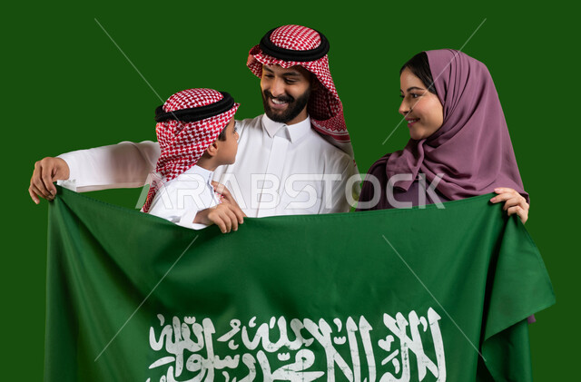 الوفاء والاخلاص للمملكة، تعليم الأبناء تقدير وحب الوطن، بورتريه لعائلة عربية خليجية سعودية سعيدة تحتفل باليوم الوطني 23 سبتمبر، الامساك بعلم السعودية بسعادة وفخر، العيد الوطني السعودي، يوم العلم السعودي 11 مارس، الإنتماء للدولة وحب البلاد، كروما، خلفية خضراء