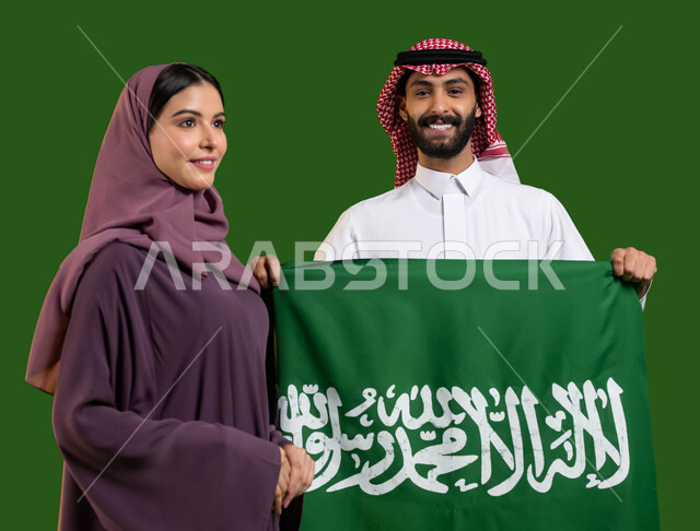Deepening belonging to the homeland by celebrating the anniversary of the National Day, September 23, a portrait of a Saudi Arabian Gulf man and woman with gestures of pleasure and happiness, a Saudi citizen holding the Saudi flag with pride, Saudi National Day, Flag Day March 11, Saudi National Day, chrome, green background