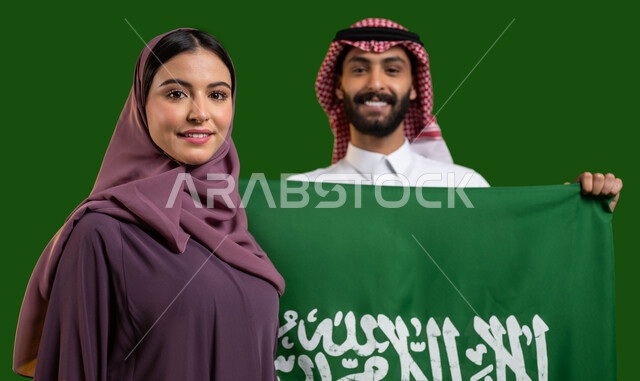 شاب سعودي يمسك علم السعودية بفخر واعتزاز، بورتريه لمواطن ومواطنة عربيان خليجيان سعوديان يحتفلان بالعيد الوطني 23 سبتمبر، إظهار مشاعر الحب والولاء للمملكة، تعميق الانتماء للوطن بالاحتفال بذكرى اليوم الوطني السعودي، يوم العلم 11 مارس، كروما، خلفية خضراء