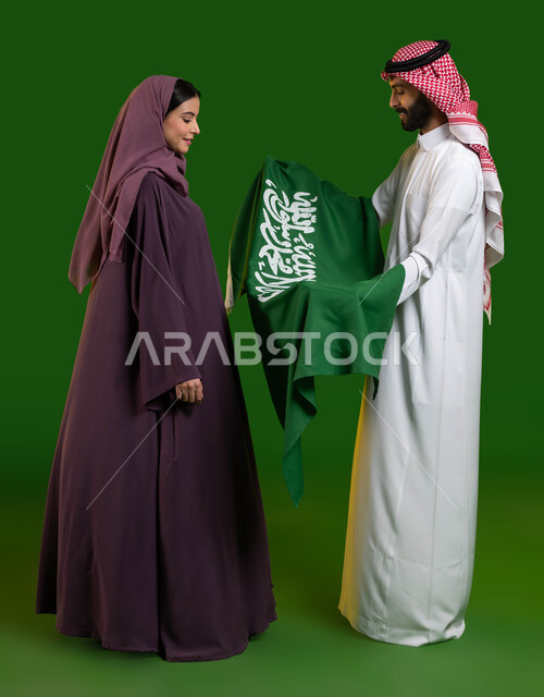 Looking at the Saudi flag with pride and pride, portrait of a Saudi Gulf Arab couple celebrating Saudi National Day, looking at the Saudi flag with pride and pride, anniversary of the reunification of the nation, National Day 8 Rabi’ al-Awwal, Flag Day March 11, full-length body portrait, chroma, green background