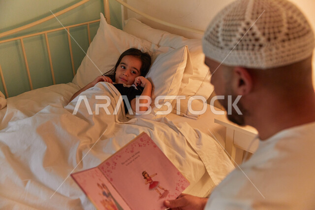 رواية الحكايات المفيده للأبناء قبل النوم، أب عربي خليجي إماراتي يرتدي الكندوره والطاقيه الاماراتيه يقوم بقراءة القصص المسليه لابنته، مفهوم الترابط الأسري، الشعور بالأمان والحب مع العائله.
