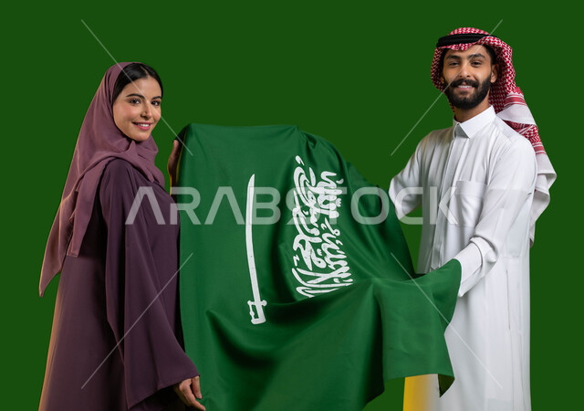 الفخر والاعتزاز بالهوية الوطنية، بورتريه لزوجان عربيان خليجيان سعوديان يحملان علم المملكة، اليوم الوطني 8 ربيع الأول، الاحتفال بيوم العلم السعودي 11 مارس، العيد الوطني السعودي، التباهي بالإنتماء للمملكة، المناسبات و الأعياد الوطنية، كروما، خلفية خضراء