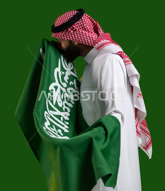 تعميق الانتماء للوطن بالاحتفال باليوم الوطني السعودي، بورتريه لشاب عربي خليجي سعودي يرتدي الشماغ والثوب التقليدي ويقوم بتقبيل علم السعودية، يوم العلم 11 مارس، العيد الوطني 8 ربيع الأول، مفهوم الإخلاض والتضحية والوفاء للمملكة، كروما، خلفية خضراء