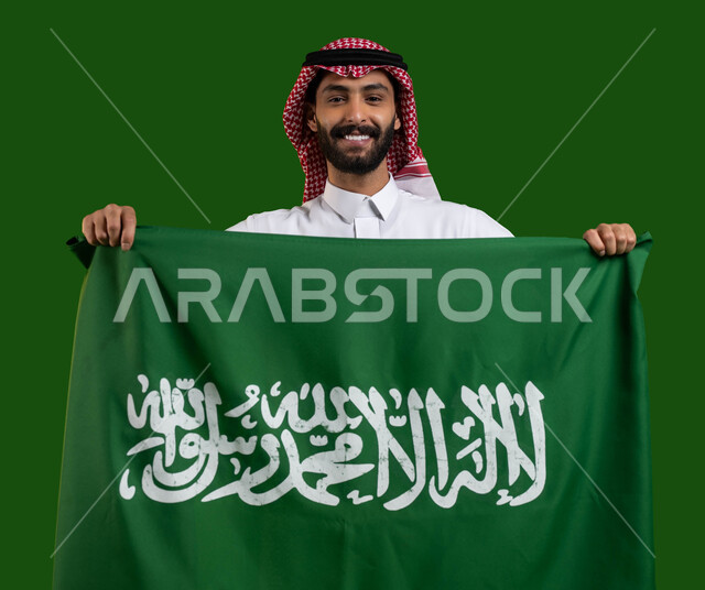 الاحتفال باليوم الوطني السعودي، بورتريه لشاب عربي خليجي سعودي مبتسم يرتدي الشماغ والثوب التقليدي ويمسك علم المملكة، يوم العلم 11 مارس، العيد الوطني 8 ربيع الأول، ايماءات السعاده والفخر بالانتماء للهوية الوطنية السعودية، كروما، خلفية خضراء