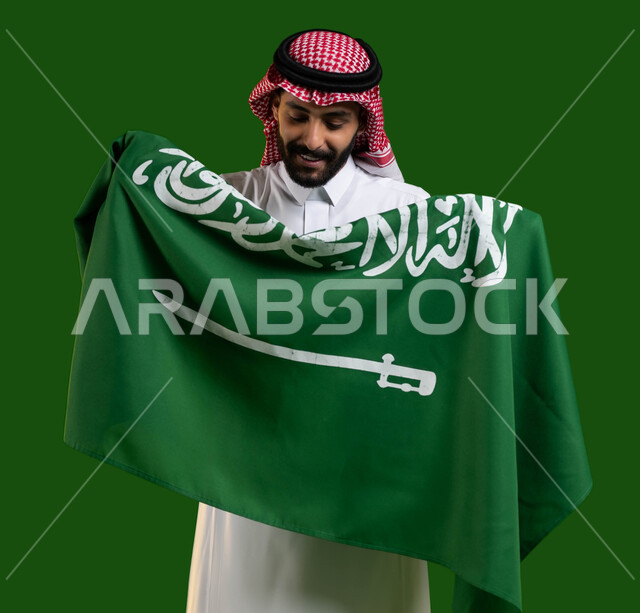 العيد الوطني السعودي 8 ربيع الأول، المشاركة بالمناسبات و الأعياد الوطنية، بورتريه لمواطن عربي خليجي سعودي يرتدي الشماغ والثوب التقليدي ويحمل علم السعودية وينظر اليه بفخر وتباهي، ذكرى اليوم الوطني لتوحيد المملكة، يوم العلم 11 مارس، كروما، خلفية خضراء