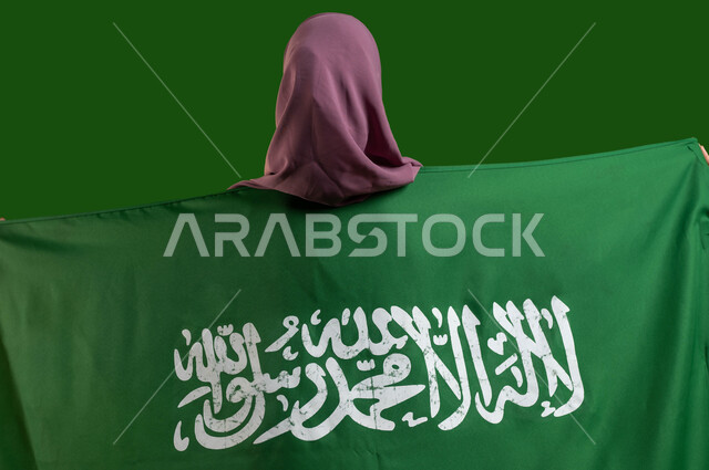 مفهوم الافتخار والاعتزاز بالوطن، بورتريه من الخلف لمواطنة عربية خليجية سعودية محجبة تضع علم السعودية على ظهرها، مشاعر الانتماء والحب للبلاد، يوم العلم السعودي 11 مارس، الإحتفال بالعيد الوطني 23 سبتمبر، ذكرى اليوم الوطني السعودي، كروما، خلفية خضراء