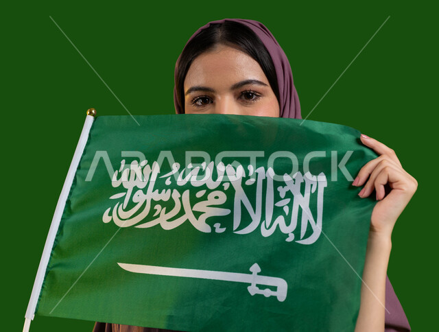 الفخر والتباهي بالهوية الوطنية، الإحتفال بيوم العلم 11 مارس، الأعياد والمناسبات الوطنية السعودية، بورتريه لامرأة عربية سعودية خليجية محجبة تقوم بتغطية وجهها بعلم المملكة، إحياء ذكرى اليوم الوطني السعودي 23 سبتمبر، العيد الوطني السعودي، كروما، خلفية خضراء