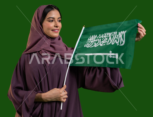 إظهار الحب والولاء للدولة، بورتريه لمواطنة عربية خليجية سعودية محجبة تسمك العلم السعودي وتنظر إليه بايماءات الفخر والاعتزاز بالوطن، اليوم الوطني السعودي، اليوم الوطني 8 ربيع الأول، الاحتفال باليوم العلم 11 مارس، التضحية والوفاء للمملكة، كروما، خلفية خضراء