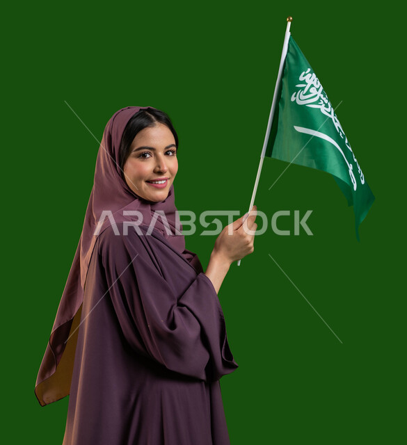 العيد الوطني 8 ربيع الأول، بورتريه من الجانب لامرأة عربية خليجية سعودية محجبة ترتدي العباءة ترتدي العباءة وتقوم بالتلويح بعلم المملكة بسرور والسعادة، يوم العلم السعودي 11 مارس، اليوم الوطني السعودي، تعميق الانتماء والولاء للوطن، كروما، خلفية خضراء