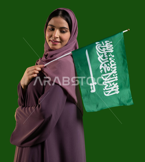 العيد الوطني لتوحيد المملكة 23 سبتمبر، بورتريه من الجانب لمواطنة عربية خليجية سعودية محجبة ترتدي العباية وتضع علم السعودية على كتفها بسرور والسعادة، يوم العلم السعودي 11 مارس، ذكرى اليوم الوطني السعودي، صورة الجسم بالطول الكامل، كروما، خلفية خضراء