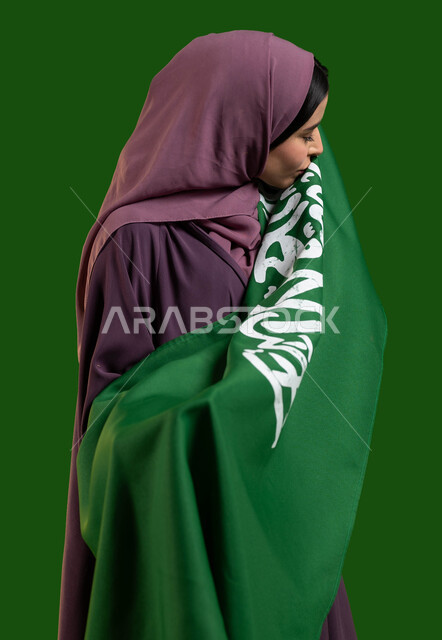 مفهوم الإخلاض والتضحية والوفاء للمملكة، بورتريه من الجانب لامرأة عربية خليجية سعودية محجبة ترتدي العباءة وتقوم بتقبيل علم السعودية، اليوم الوطني السعودي، العيد الوطني 23 سبتمبر، يوم العلم السعودي 11 مارس، الاحتفال بالاعياد الوطنية، كروما، خلفية خضراء