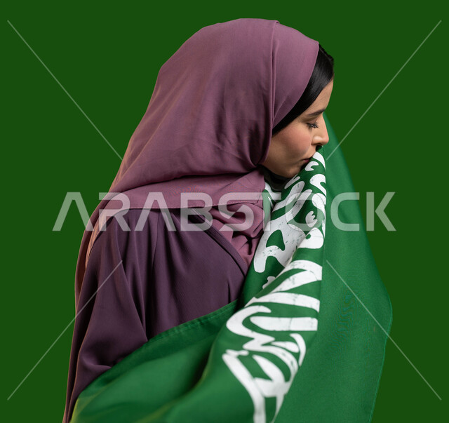 الشغف وحب المملكة والإنتماء إليه، بورتريه من الجانب لمواطنة عربية خليجية سعودية محجبة ترتدي العباءة وتقوم بتقبيل علم السعودية، تعميق الإنتماء للوطن والإحتفال باليوم الوطني السعودي، العيد الوطني 8 ربيع الأول، يوم العلم السعودي 11 مارس، كروما، خلفية خضراء