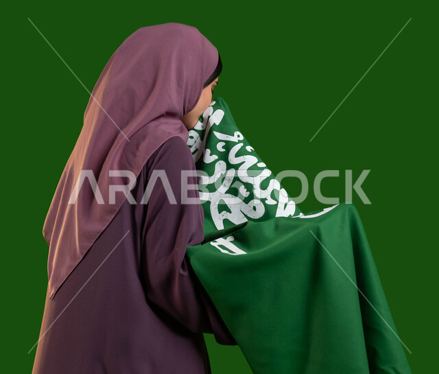 الفخر والاعتزاز بالهوية الوطنية، بورتريه من الجانب لامرأة عربية خليجية سعودية محجبة تقوم بتقبيل علم المملكة، يوم العلم السعودي 11 مارس، الاحتفال باليوم الوطني السعودي، العيد الوطني 8 ربيع الأول، مشاعر الانتماء للوطن، كروما، خلفية خضراء