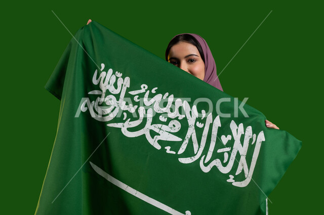 الإنتماء للوطن وحب البلاد، بورتريه لمواطنة عربية خليجية سعودية محجبة تقوم بتغطية وجهها بعلم السعودية، الإحتفال باليوم الوطني السعودي 8 ربيع الأول، ذكرى العيد الوطني لتوحيد المملكة، يوم العلم السعودي 11 مارس، المشاركة بالمناسبات الوطنية، كروما، خلفية خضراء