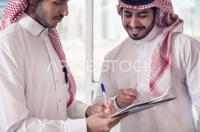 رجال اعمال سعوديين يتحدثون و يتناقشون في عقد العمل في مقر الشركة ، توقيع عقد عمل ،اتفاقية و صفقة جديدة ، شركاء عمل ، بيئة العمل