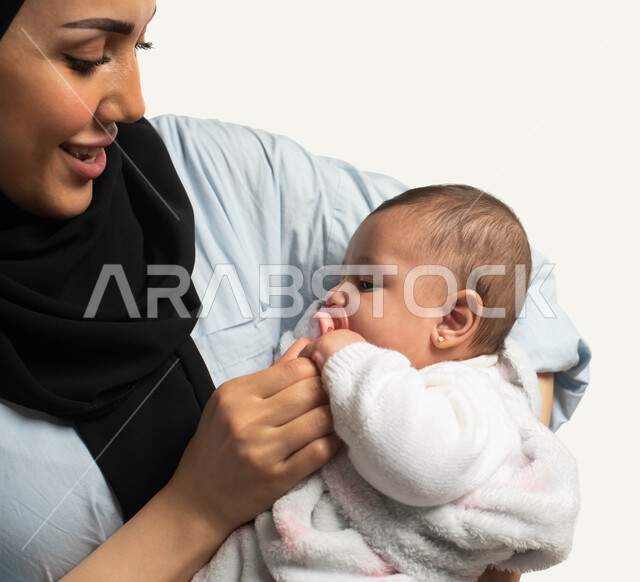 الاعتناء والاهتمام بالأبناء الرضع, النظر إلى الطفلة بإيماءات الحنان والحب, بورتريه مقرب لأم عربيه خليجية سعوديه تقوم بوضع اللهاية لابنتها, استخدام الادوات لتهدئة واسترخاء الأطفال, أهميه ودور الأم تجاه أولادها, خلفيه بيضاء