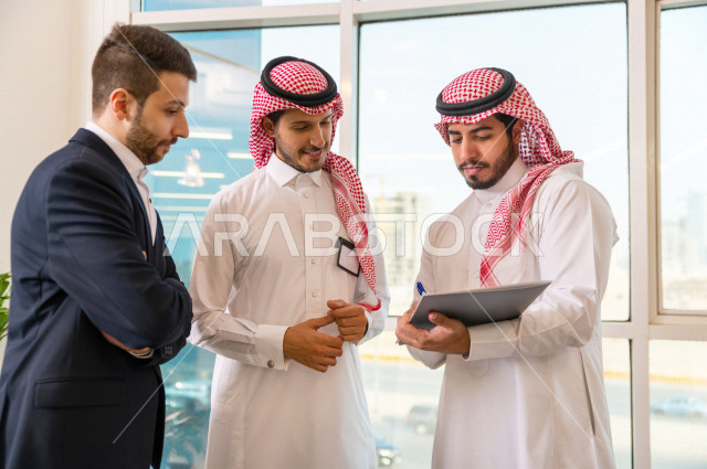 مجموعة من رجال الأعمال الرياديون الخليجيون ، احدهم من جنسية مختلفة يرتدي البدلة الرسمية ، ادارة الاعمال داخل مقر الشركة ، شركة سعودية ، بيئة العمل
