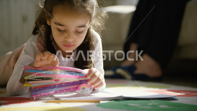 استغلال أوقات الفراغ بالأنشطة الترفيهية الممتعة, صورة مقربة لفتاة عربية خليجية إماراتية تجلس على الأرض وتقوم باستخدام أقلام التلوين, تنمية مهارات الأولاد الذهنية والحركية, رعاية الأبناء والاهتمام بالهوايات المفيدة