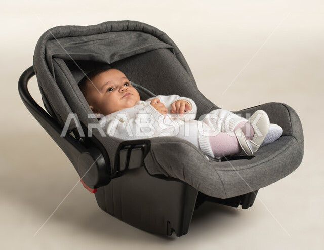 ايماءات النظر إلى شيء ما ,مفهوم النعومة و البراءة و الطفولة, بورتريه لطفلة عربيه خليجيه سعودية لطيفة ترتدي لباس أبيض قطني تجلس في الكرسي الخاص بها , خلفية بيضاء