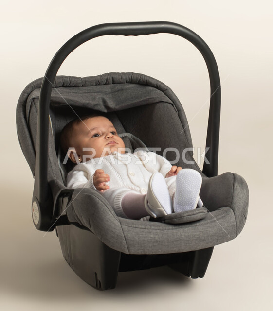 ايماءات النظر إلى شيء ما ,مفهوم البراءة و الطفولة, بورتريه لطفلة عربيه خليجيه سعودية لطيفة ترتدي لباس أبيض قطني تجلس في الكرسي الخاص بها , خلفية بيضاء