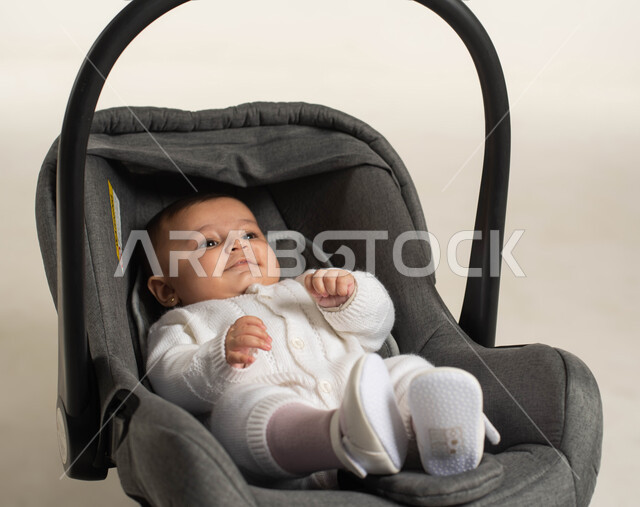 Gestures of play and happiness, the concept of innocence and childhood, a portrait of a cute Saudi Arabian Gulf girl wearing a white cotton dress sitting in her chair, white background