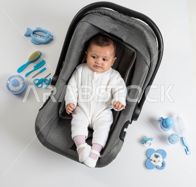 ايماءات الغضب والانزعاج, الاعتناء بصحة الأبناء والاهتمام بهم, بورتريه لطفلة عربيه خليجيه سعودية لطيفة ترتدي لباس أبيض قطني تجلس في الكرسي الخاص بها , أدوات الرضاعه ومستلزمات الرضيع, خلفية بيضاء