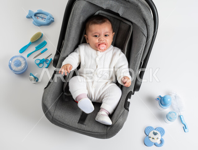 توفير الأدوات اللازمة للعناية بالطفل ,الاعتناء بصحة الأبناء والاهتمام بهم, استخدام اللهاية للاسترخاء والنوم, بورتريه لطفلة عربيه خليجيه سعودية لطيفة ترتدي لباس أبيض قطني تجلس في الكرسي الخاص بها , خلفية بيضاء