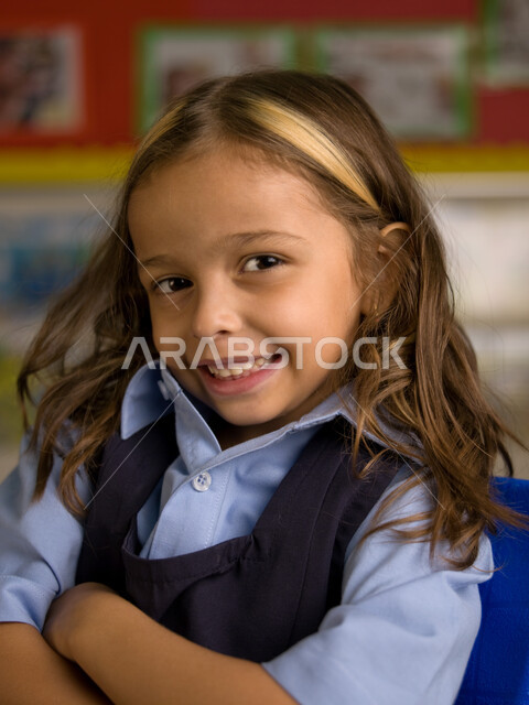 المدارس الأكاديمية في الإمارات العربية، الاستعداد للعام الدراسي الجديد، التقاط صور شخصية للطلاب لتجهيز البطاقات التعريفية، صوره مقربة لفتاة عربية خليجية إماراتية ترتدي الزي المدرسي مبتسمة تنظر إلى الكاميرا، إيماءات وجه تدل السعادة بالعودة إلى المدرسة.