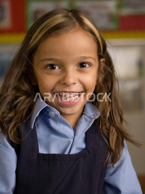 المدارس الأكاديمية في الإمارات العربية، الاستعداد للعام الدراسي الجديد، التقاط صور شخصية للطلاب لتجهيز البطاقات التعريفية، صوره مقربة لفتاة عربية خليجية إماراتية ترتدي الزي المدرسي مبتسمة تنظر إلى الكاميرا، إيماءات وجه تدل السعادة بالعودة إلى المدرسة.