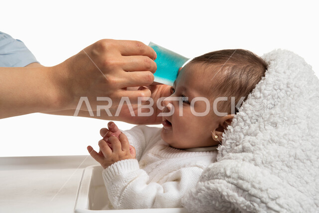 Health care and the concept of caring for children, performing medical home treatments, a Saudi Arabian Gulf woman using a fever-reducing gel compress, a close-up portrait of a sick girl with a fever sitting on a children’s chair, gestures of calm and a sense of security, white background.