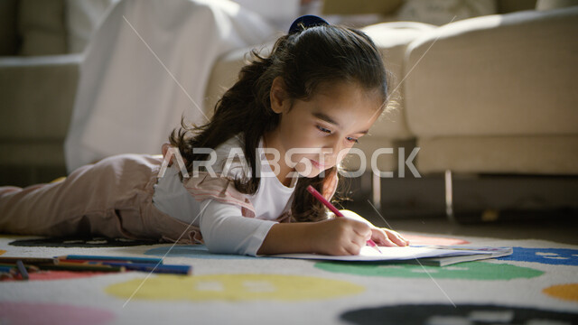  قضاء أوقات ممتعه في  العطلة الصيفيه، صورة مقربة لفتاة عربية إماراتية خليجية مستلقية على الأرض تحمل بيدها قلم التلوين، استغلال وقت الفراغ في القيام بأنشطة ترفيهيه ،تنمية المهارات والقدرات الذهنية، حل الواجبات المدرسية في المنزل